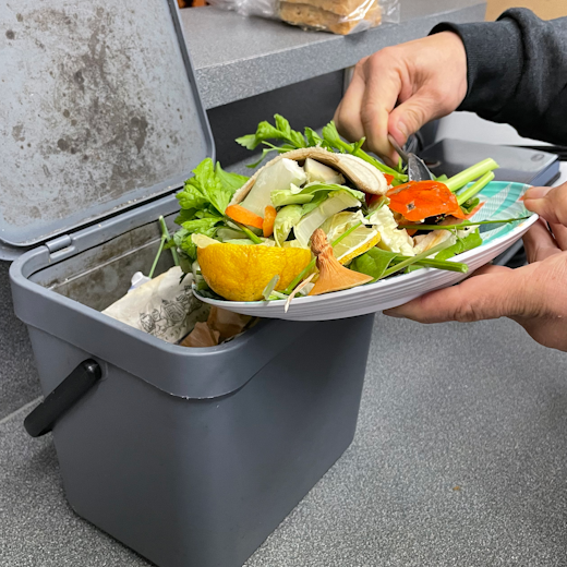 A plate of vegetable and fruit scraps being put into a compost caddy.